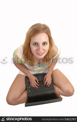 Apretty teenage girl, sitting on the floor with a laptop, looking up to thecamera, smiling, with blond hair and white shorts, over white background.