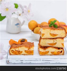 apricot biscuit cake cut into square pieces on a white wooden board