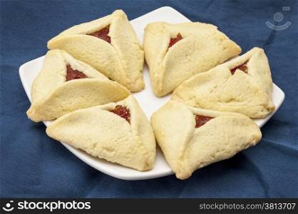 apricot hamantaschen cookies on a plate against blue tablecloth - a traditional pastry in Ashkenazi Jewish cuisine for holiday of Purim