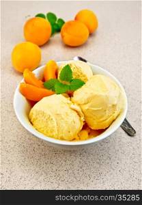 Apricot ice cream in a white bowl with slices of fruit and mint on a background granite table