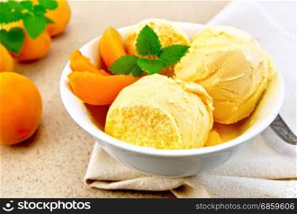 Apricot ice cream in a white bowl with slices of fruit, mint and spoon on a napkin on a granite background table