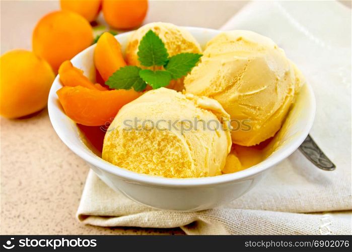 Apricot ice cream in a white bowl with slices of fruit, spoon on a napkin on a background granite table