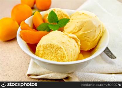 Apricot ice cream in a white bowl with slices of fruit, spoon on a napkin on a background granite table