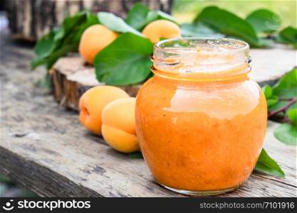 Apricot jam in a glass jar and ripe apricots on a wooden table. Close-up.. Apricot jam in a glass jar and ripe apricots on a wooden table.