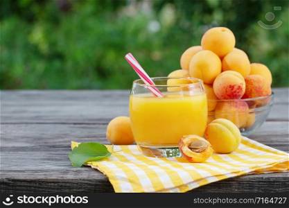 Apricot juice in glass and apricots on wooden table. Checkered yellow napkin. Green natural background. Apricot juice in glass and apricots on wooden table