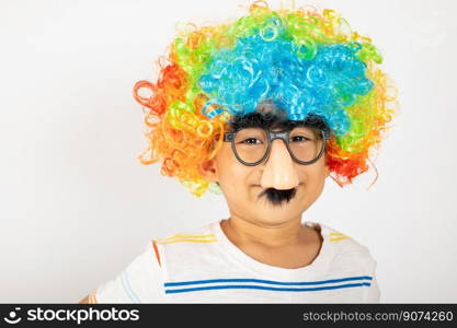 April Fool’s Day. Portrait of Funny kid boy clown wears a curly wig colorful a big nos and glasses and has a mustache isolated on white background with copy space, Happy child festive decor