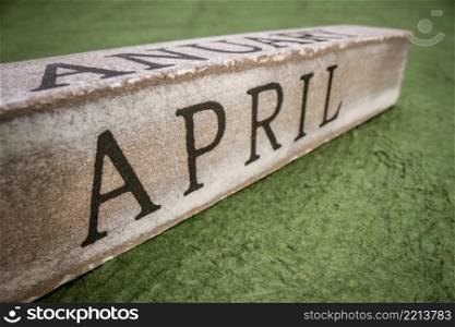 April text on grunge wooden block against handmade textured paper, calendar concept