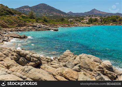 Aquamarine Mediterranean sea, rocks &amp; maquis at Cala d&rsquo;Olivu north of Ile Rousse in the Balagne region of Corsica with houses at Monticello in the background