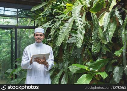 Arab business asian man using tablet,standing in green cafe wear muslim dress ,freelance business concept.