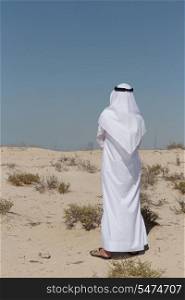 Arab man in national dress stands in the desert and looks at the city of Dubai. Arab man in the desert