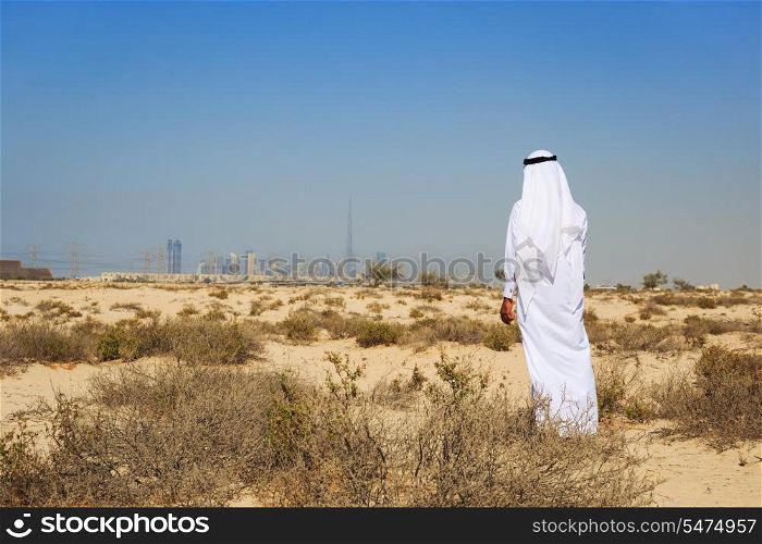 Arab man in national dress stands in the desert and looks at the city of Dubai