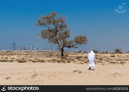 Arab man in national dress stands in the desert and looks at the city of Dubai
