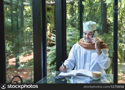 Arab muslim businessman use smartphone communication and write on book in coffee shop ,freelance no working space lifestyle.