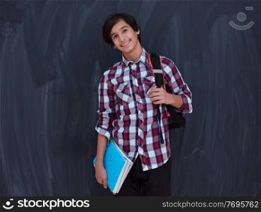 arab teenager with backpack and books wearing casual western school look against black chalkboard background