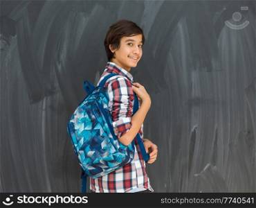 Arab teenager with backpack wearing casual school look against a black chalkboard background. High quality photo. arab teenager with backpack wearing casual school look against black chalkboard background