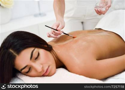 Arab woman receiving back massage treatment with oil brush in spa wellness center. Beauty and Aesthetic concepts.