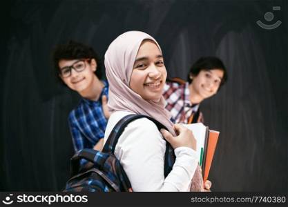 Arabic teenagers, students group portrait against black chalkboard wearing backpack and books in school.Selective focus. High quality photo. Arabic teenagers, students group portrait against black chalkboard wearing backpack and books in school.Selective focus