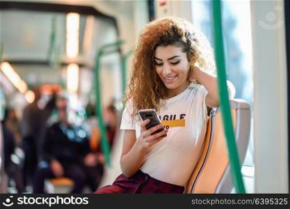 Arabic woman inside subway train looking at her smart phone. Arab girl in casual clothes.