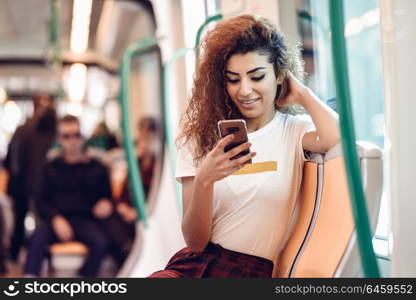 Arabic woman inside subway train looking at her smart phone. Arab girl in casual clothes.