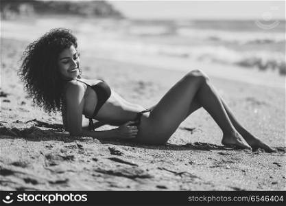 Arabic woman with beautiful body in bikini lying on the beach sa. Young arabic woman with beautiful body in swimwear lying on the beach sand. Smiling female with curly long hairstyle wearing black bikini.