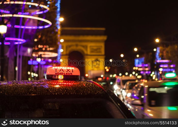 Arc of Triumph in Avenue of Champs-Elysees at night with selective focus on the taxi in the first plan