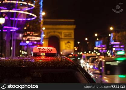 Arc of Triumph in Avenue of Champs-Elysees at night with selective focus on the taxi in the first plan