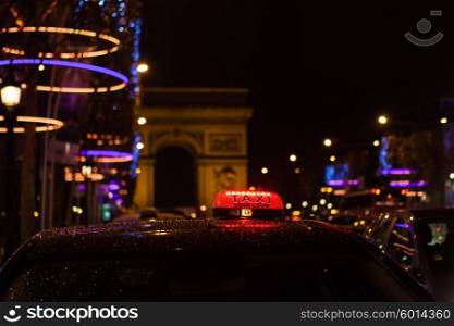 Arc of Triumph in Avenue of Champs-Elysees at night with selective focus on the taxi in the first plan