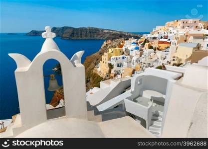 Arch with a bell, white houses and church with blue domes in Oia or Ia, island Santorini, Greece