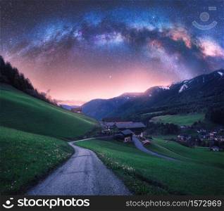 Arched Milky Way over the rural mountain road in summer in Italy. Beautiful night landscape with starry sky, milky way arch, winding road in mountain village, hills, green meadows and buildings. Space. Arched Milky Way over the rural mountain road in summer in Italy