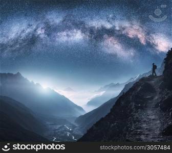 Arched Milky Way, woman and mountains at night. Silhouette of standing girl on the mountain peak, mountains in low clouds and starry sky in Nepal. Space landscape with bright milky way arch. Travel