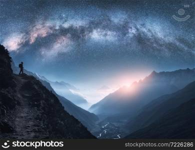 Arched Milky Way, woman and mountains at night. Silhouette of standing girl on the mountain peak, mountains in low clouds and starry sky in Nepal. Space landscape with bright milky way arch. Travel