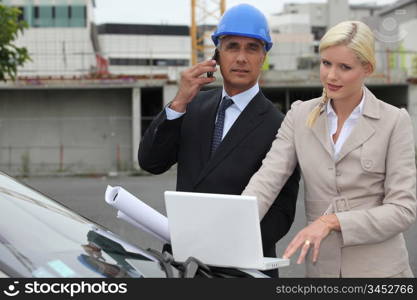 Architect and assistant stood by car with plan