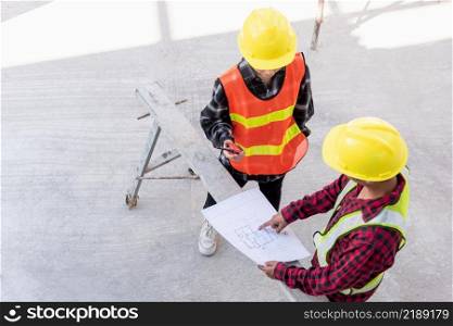 Architect and client discussing help create plan with blueprint of the building at construction site floor. Asian engineer foreman worker man and woman meeting and planning construction work, top view