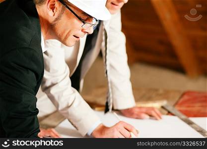 Architect and construction engineer or surveyor discussion plans and blueprints. Both are wearing hardhats and are standing on the construction site of a home indoors