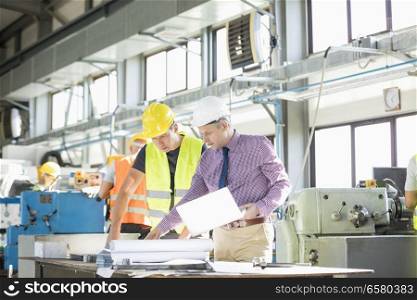 Architect and manual worker examining blueprint at table in industry