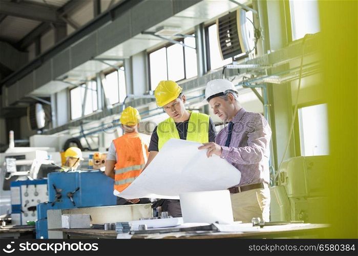 Architect and manual worker reading blueprint at table in industry