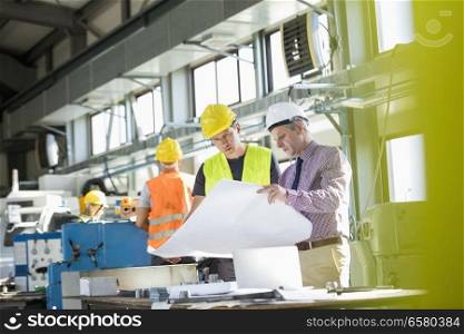 Architect and manual worker reading blueprint at table in industry