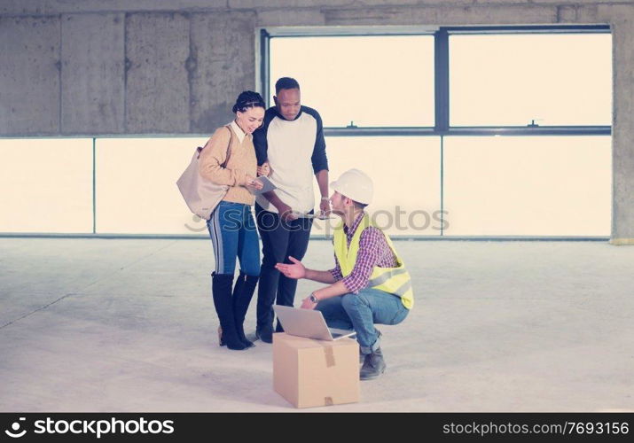 architect engineer using laptop computer while showing house design plans to a young multiethnic couple at construction site