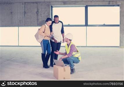 architect engineer using laptop computer while showing house design plans to a young multiethnic couple at construction site