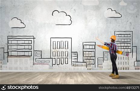 Architect female designer. Young female engineer in hard hat with big pencil and buildings sketches at background