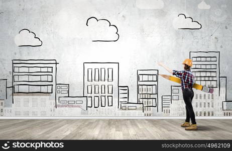 Architect female designer. Young female engineer in hard hat with big pencil and buildings sketches at background