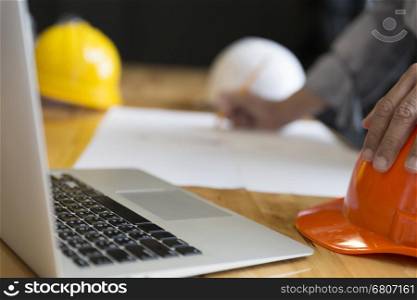 architect holding pencil working on blueprint of construction project in workplace with computer on office desk