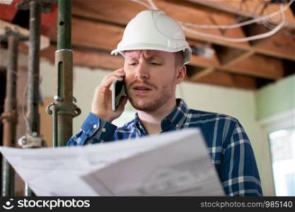 Architect Inside House Being Renovated Studying Plans Talking On Mobile Phone