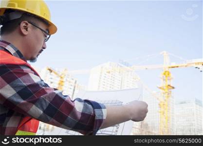 Architect looking at a blueprint outdoors at a construction site