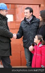 Architect shaking hands with a young family on site