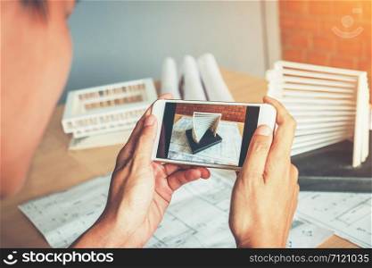 Architect using smart phone photograph model building in office