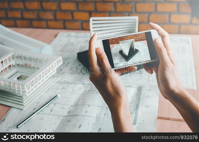 Architect using smart phone photograph model building in office.