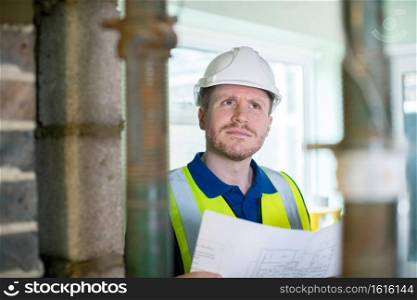Architect Wearing Hard Hat  Inside House Being Renovated Studying Plans