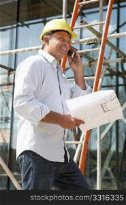 Architect With Plans Outside New Home Talking On Mobile Phone