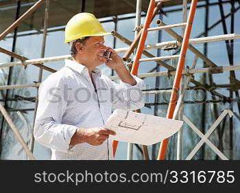 Architect With Plans Outside New Home Talking On Mobile Phone